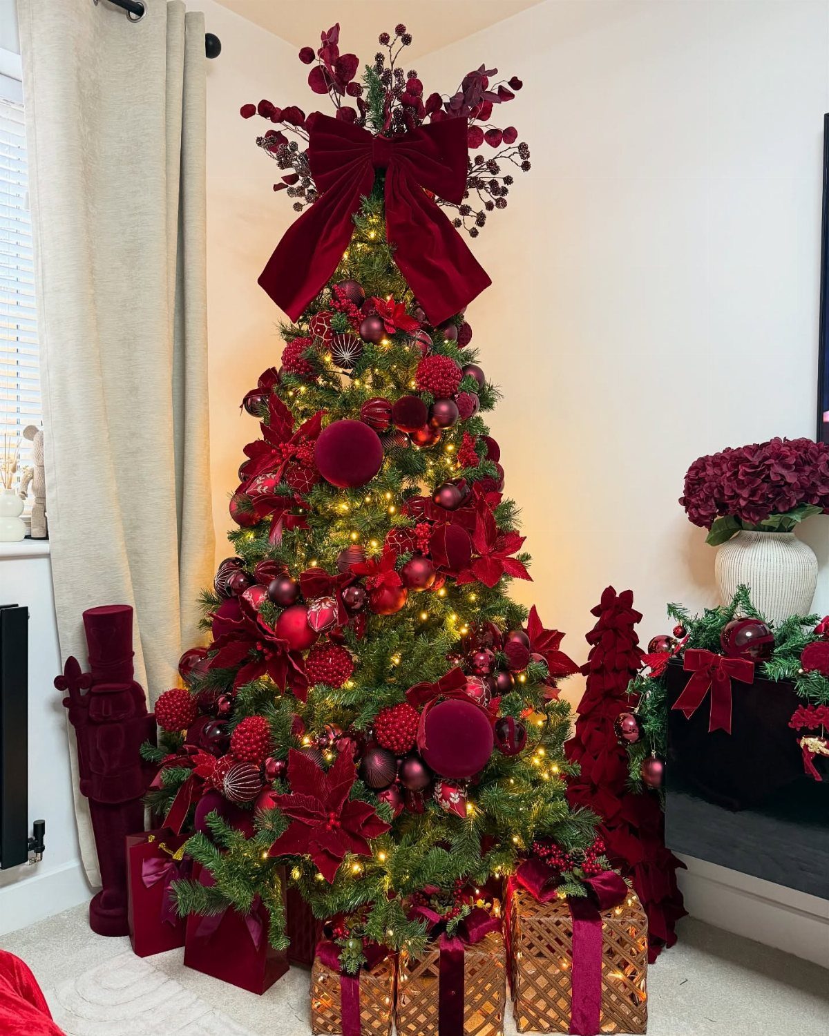 A Christmas tree decorated with burgundy ornaments, red poinsettias, and a large velvet bow.