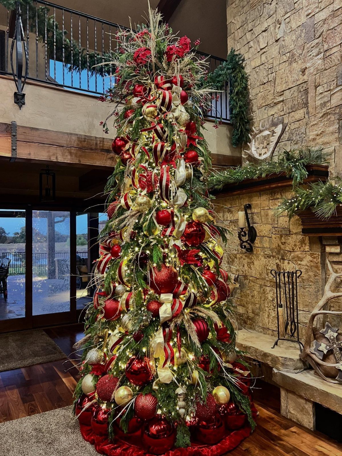 A decorated Christmas tree with red and burgundy ornaments and gold baubles in a living room.