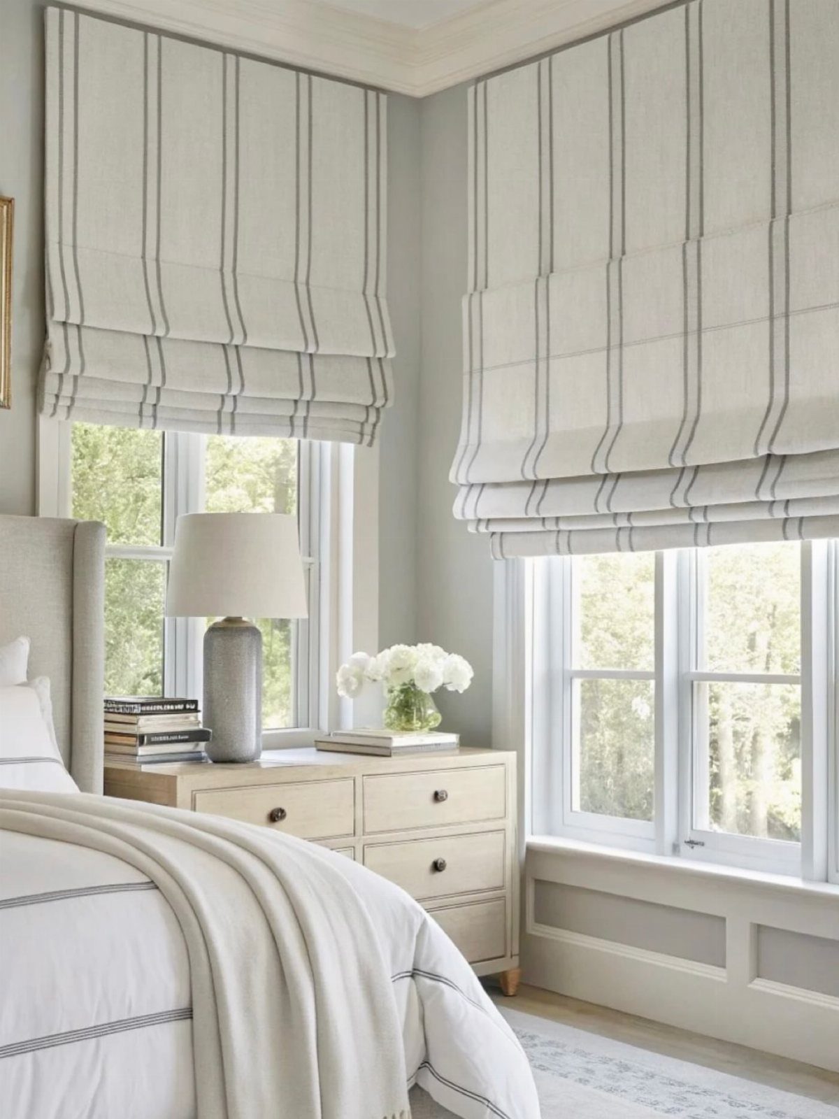Striped roman blinds hanging over windows in a bright, neutral-toned bedroom setting.