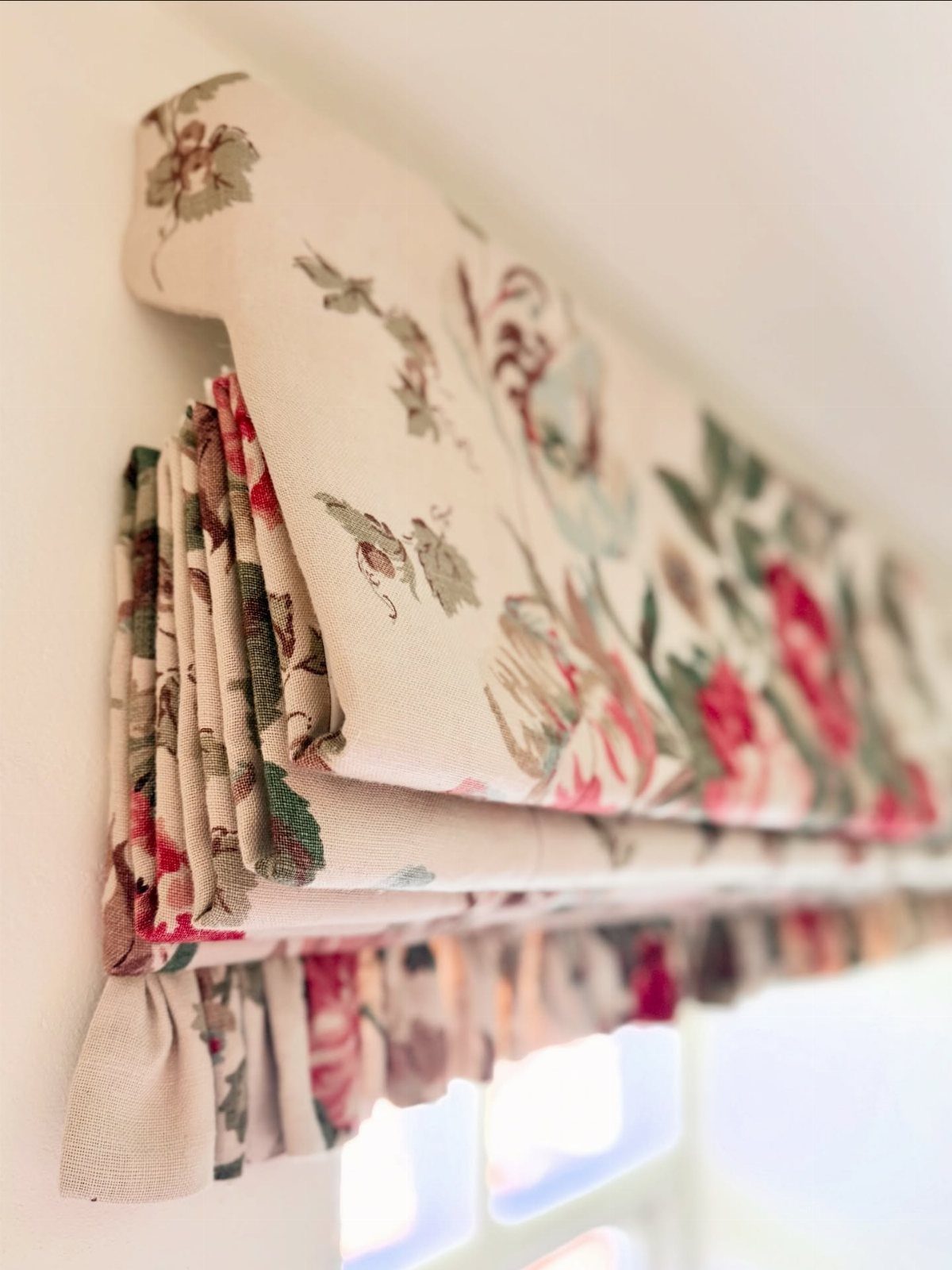 Floral patterned roman blind with large pink roses hanging over a white window frame.