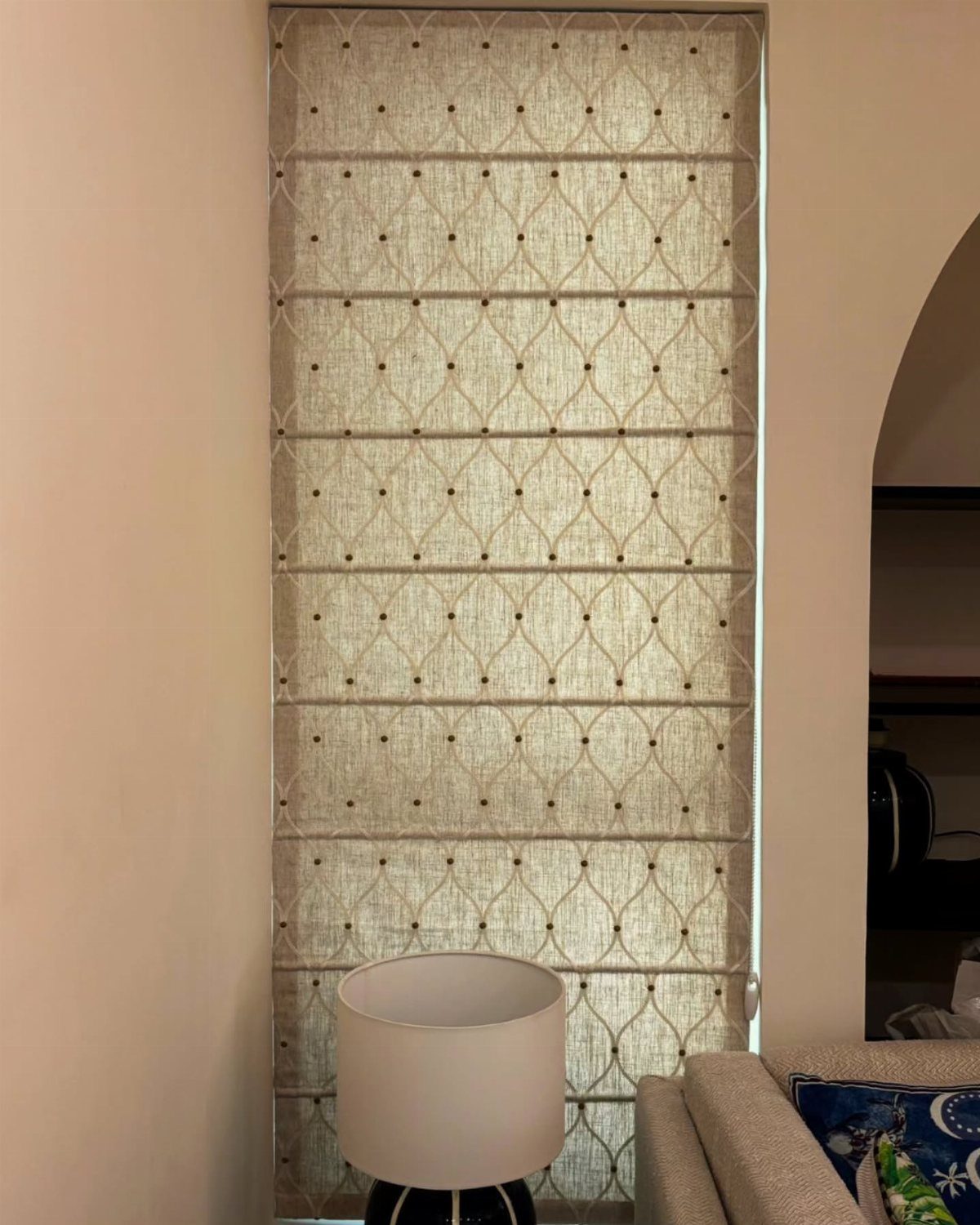 A patterned beige roman blind with a dark trellis design hanging in a window.