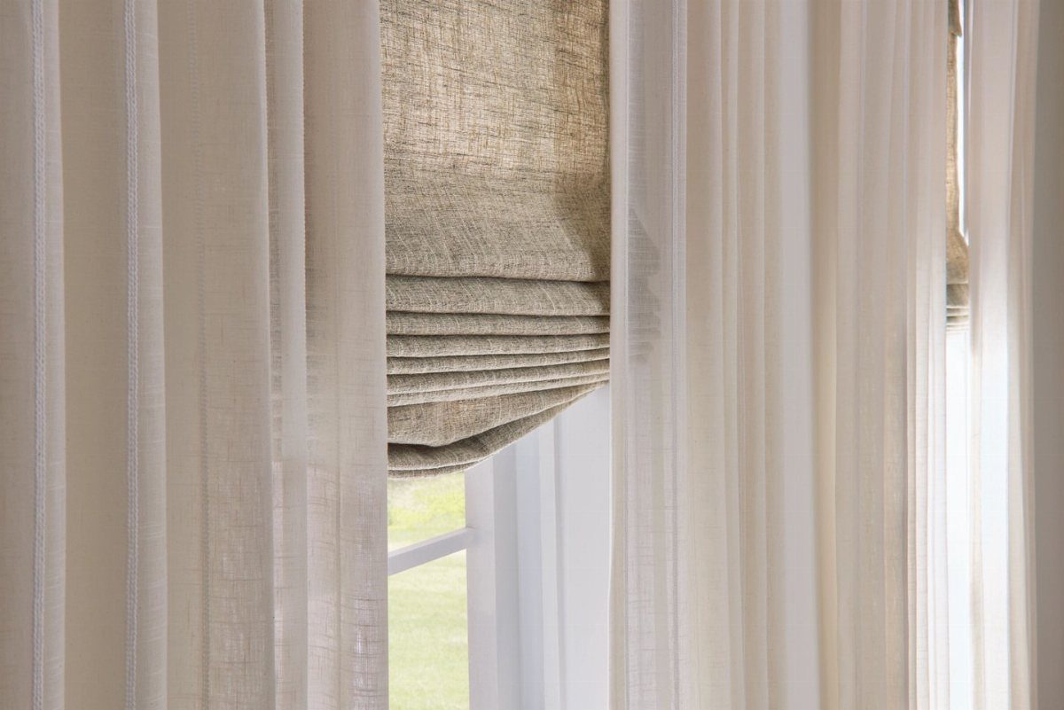 Roman Shades with Curtains: 8 Looks That Work 4 Beige linen roman shades layered behind flowing white sheer curtains on a bright window.