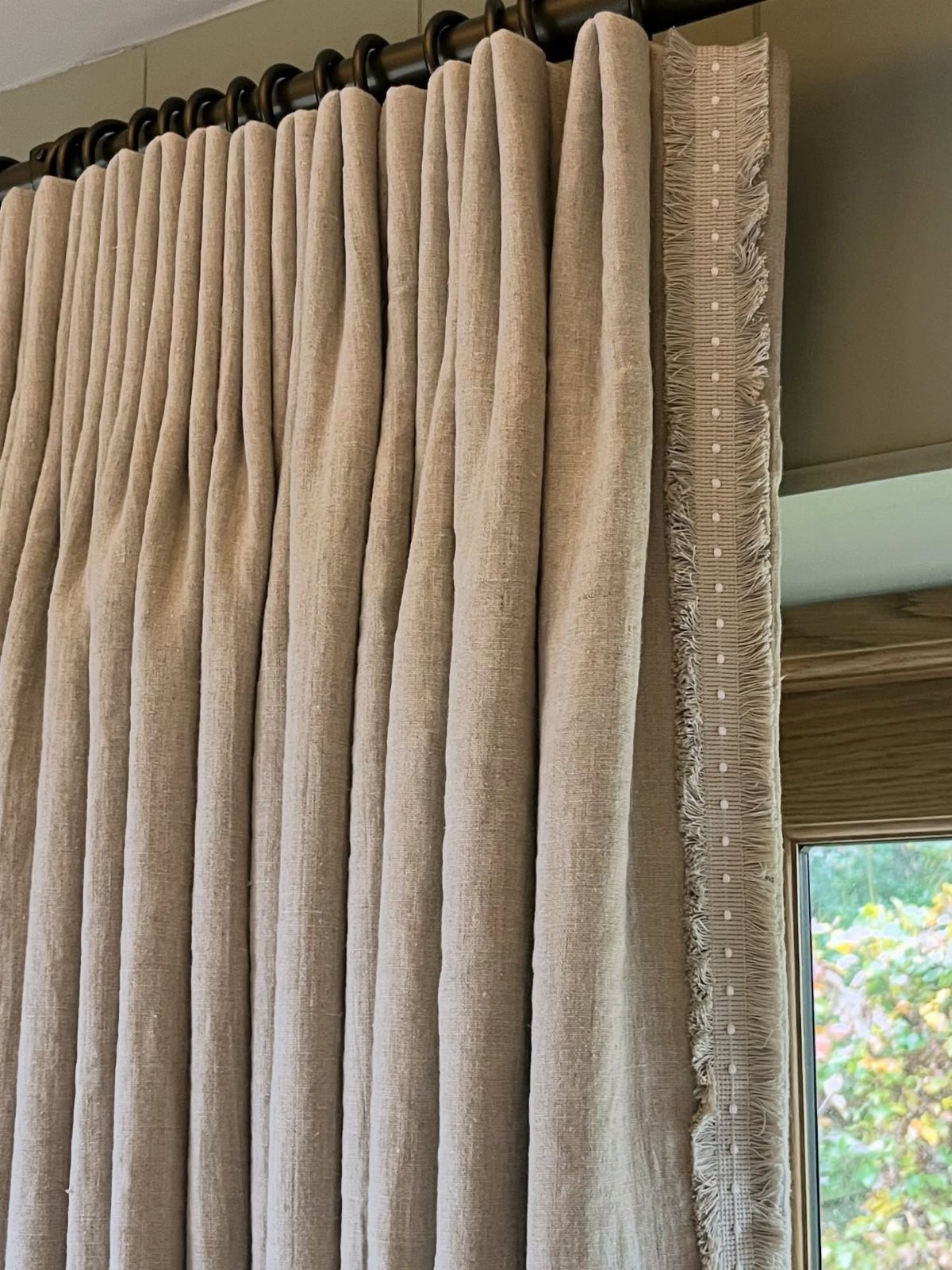 22 Unique Bedroom Curtains for Layered, Canopy and Lighted Styles 12 Beige linen curtains with a decorative fringe trim hanging from a dark metal rod.