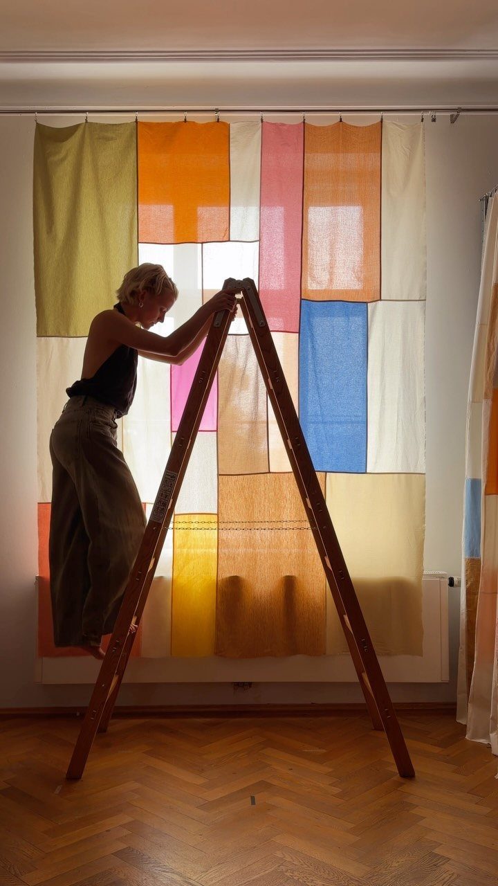22 Unique Bedroom Curtains for Layered, Canopy and Lighted Styles 5 A person on a wooden ladder hanging colorful patchwork gauze curtains in front of a window.