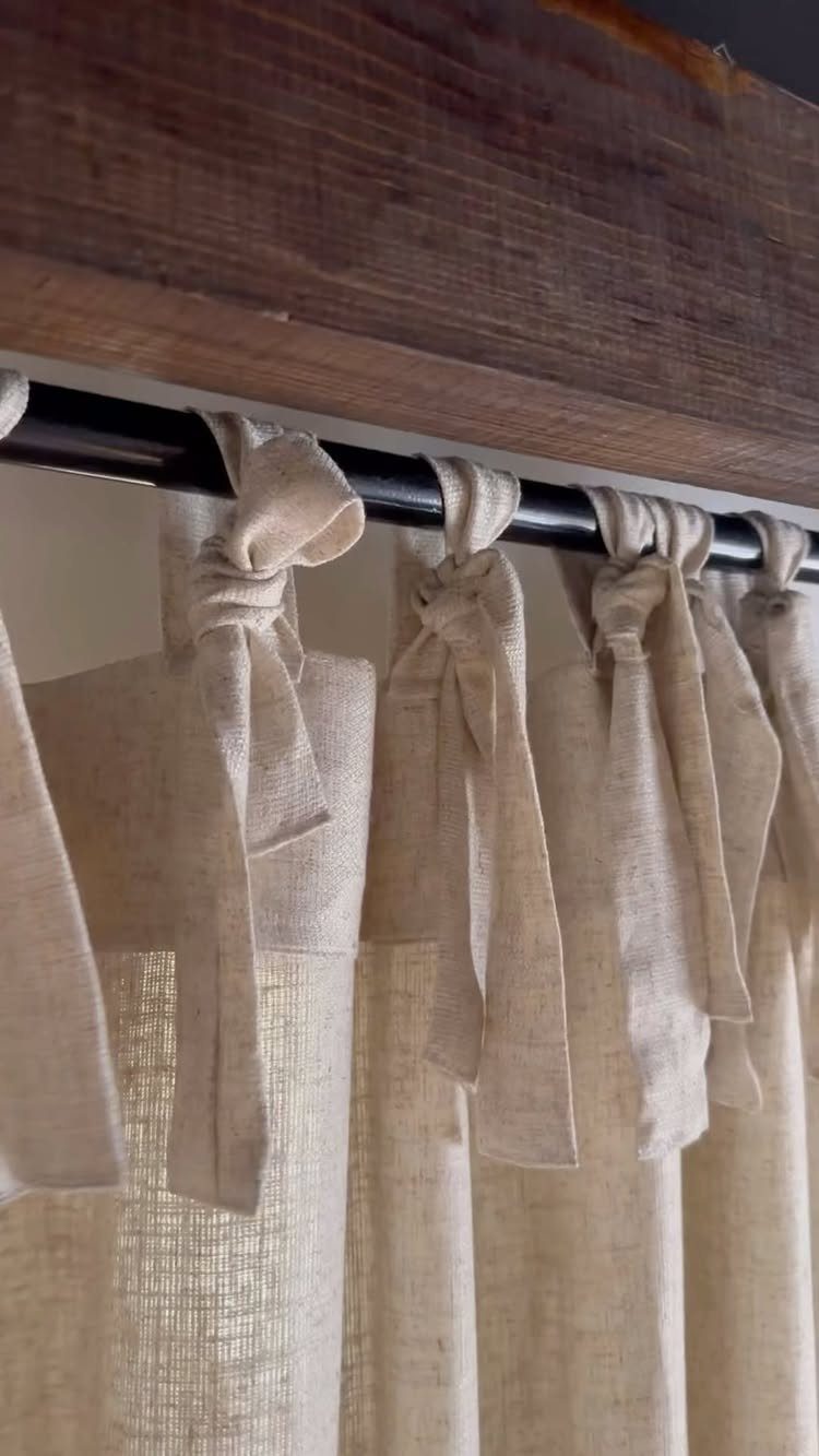 22 Unique Bedroom Curtains for Layered, Canopy and Lighted Styles 17 Beige linen curtains with large fabric tie knots hanging from a black rod.