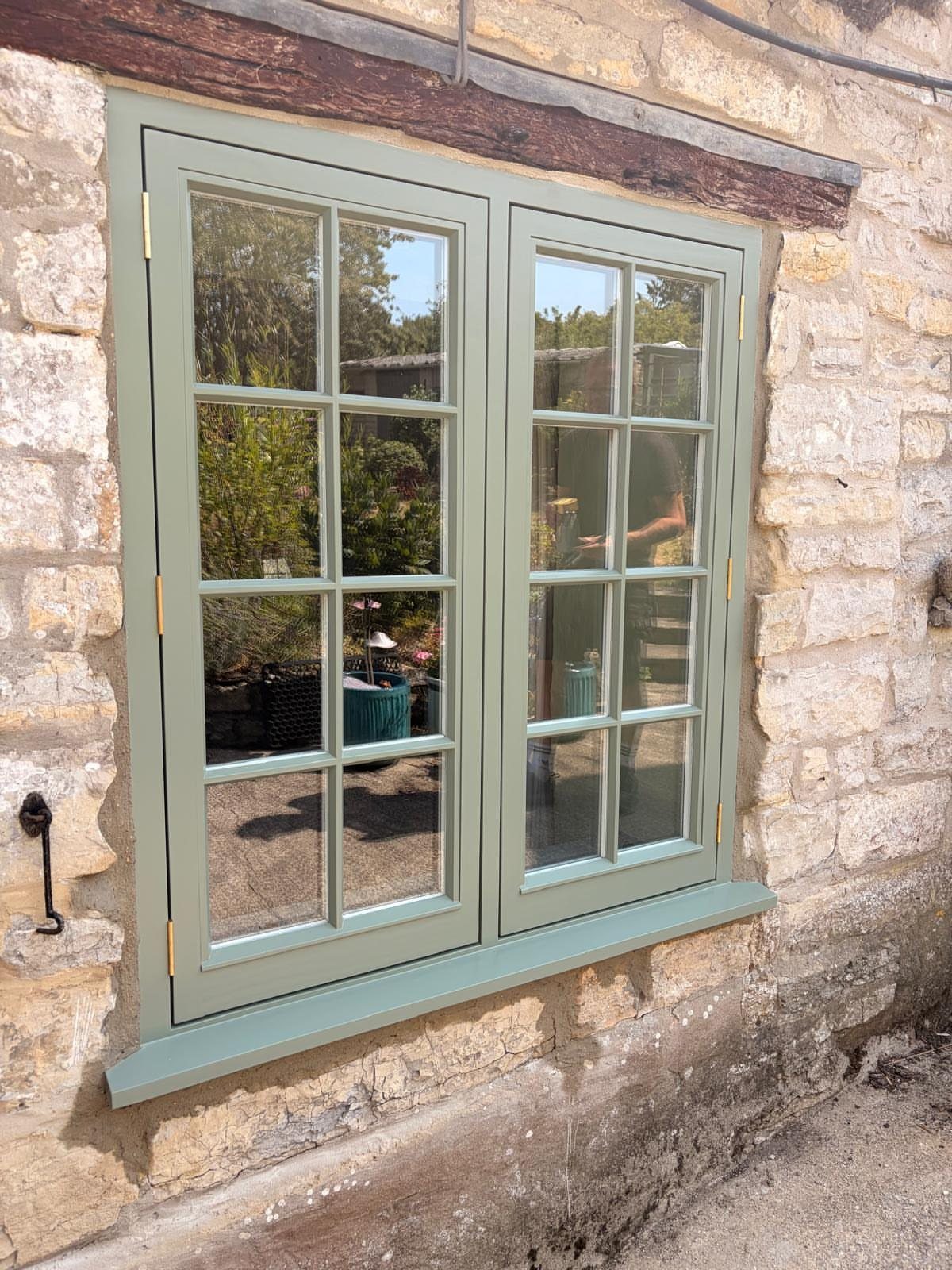 Two sage green paneled casement windows installed in a rustic stone wall.
