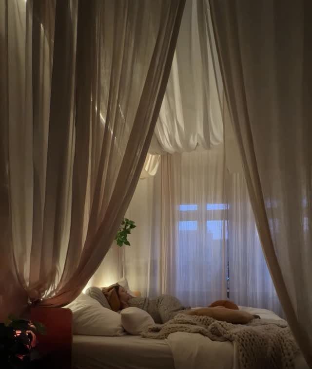 11 Ways to Style Curtains for Every Room in 2026 5 Sheer white fabric panels draped from the ceiling around a cozy bed in a dimly lit room.