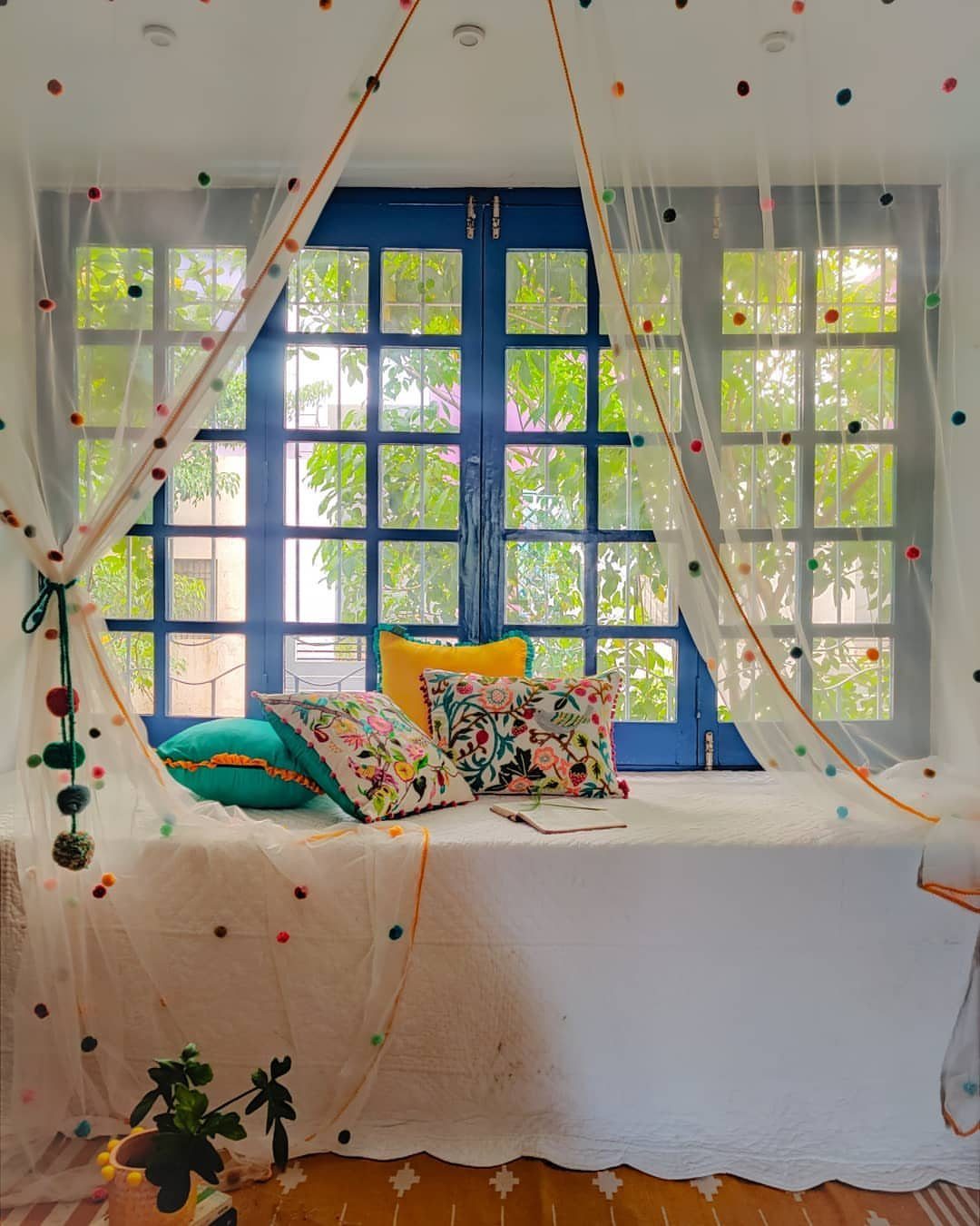 11 Ways to Style Curtains for Every Room in 2026 6 Sheer white curtains with colorful pom-poms draped over a window seat with patterned pillows.