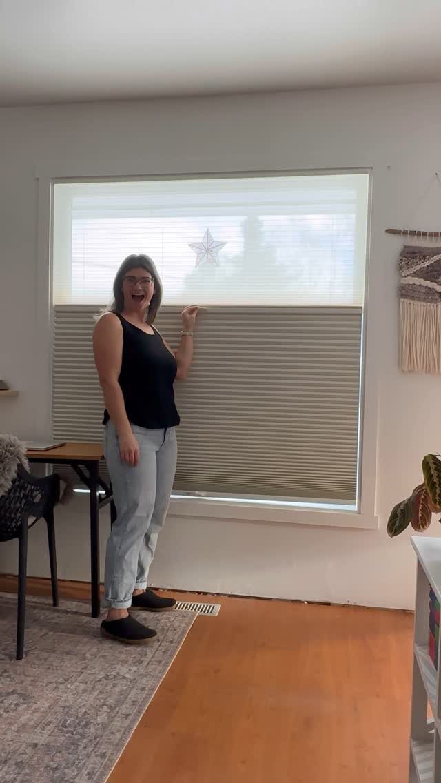 Window Blinds for Living Room: 11 Photo Ideas 9 A woman stands beside a large window with grey cellular blinds in a living room.