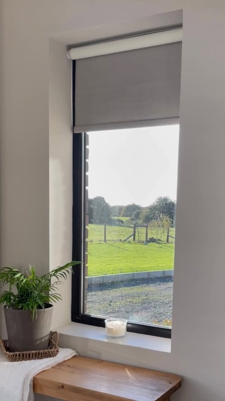 Window Blinds for Living Room: 11 Photo Ideas 5 A grey roller blind partially covering a window overlooking a green field and trees.