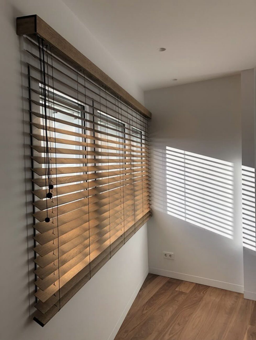Window Blinds for Living Room: 11 Photo Ideas 4 Light wood horizontal blinds covering a large window in a bright, modern room with white walls.