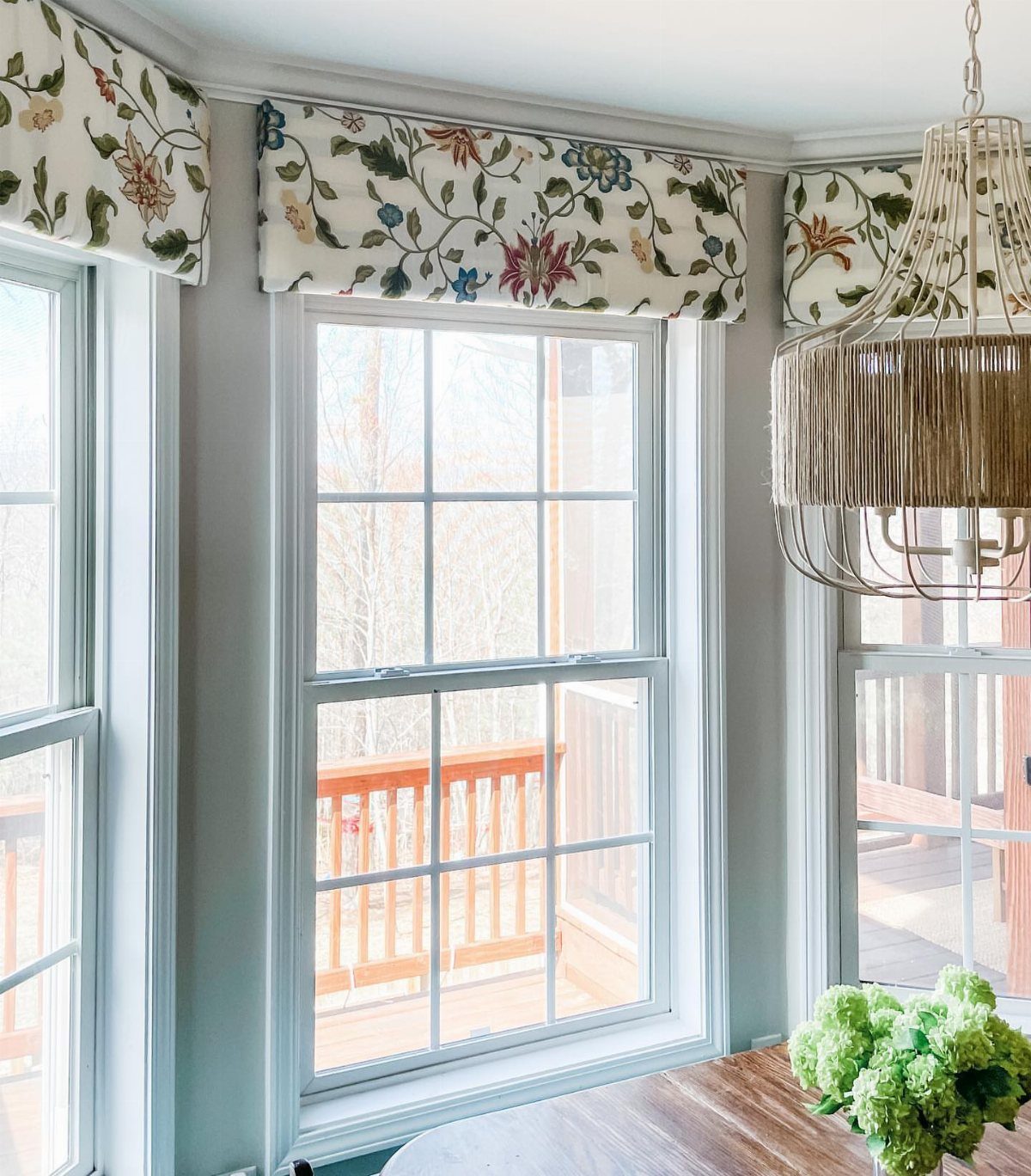 Window Cornice DIY: 5 Ways With Fabric, Wood, and Molding 4 Floral patterned fabric cornices mounted above white-framed windows in a bright room.