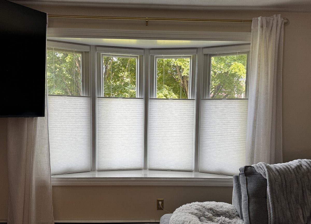 10 Window Dressing Ideas for Shutters, Shades and Blinds 9 White cellular shades covering a bay window with green trees visible through the top panes.