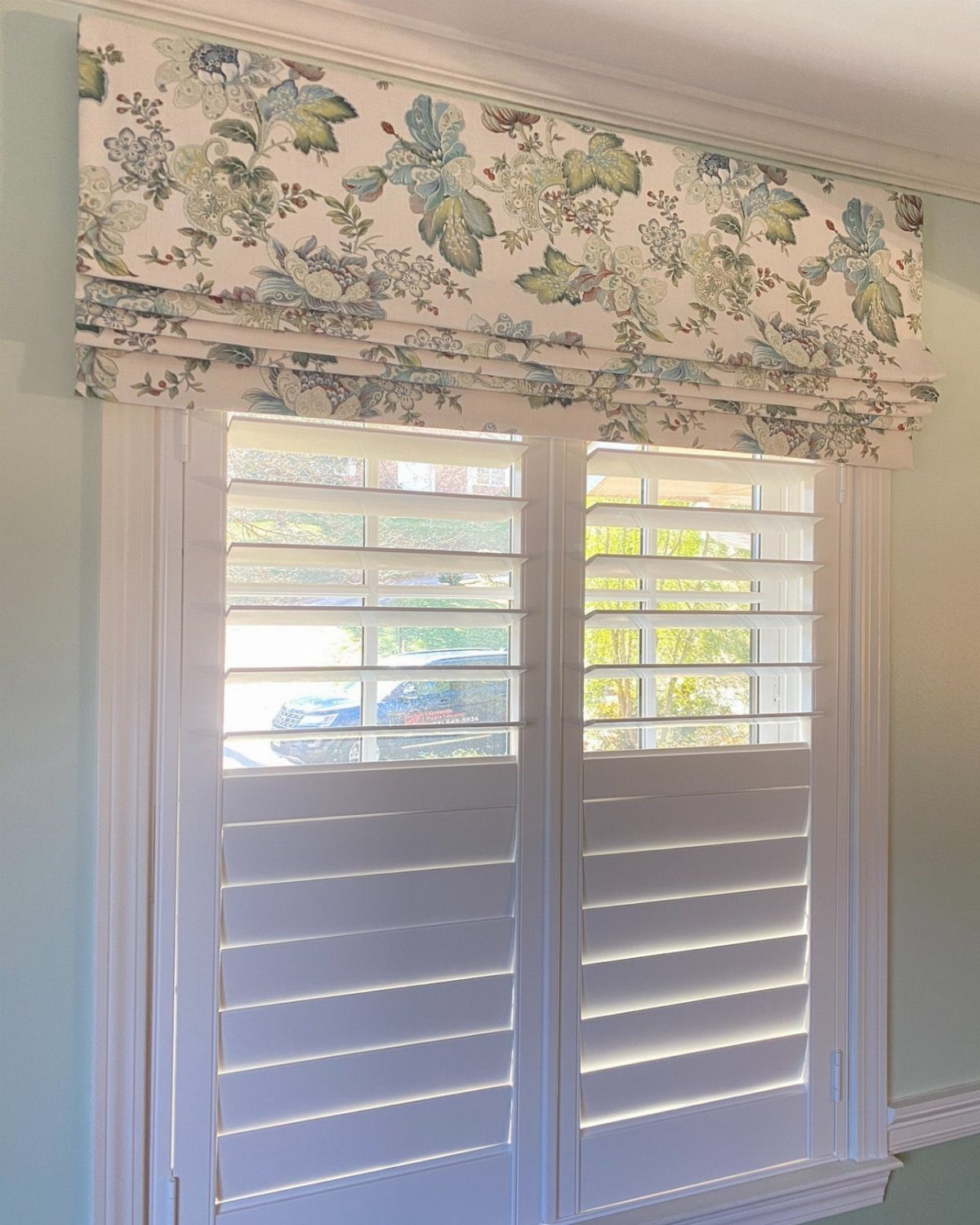 10 Window Dressing Ideas for Shutters, Shades and Blinds 10 Floral patterned fabric valance hanging above white plantation shutters on a window.