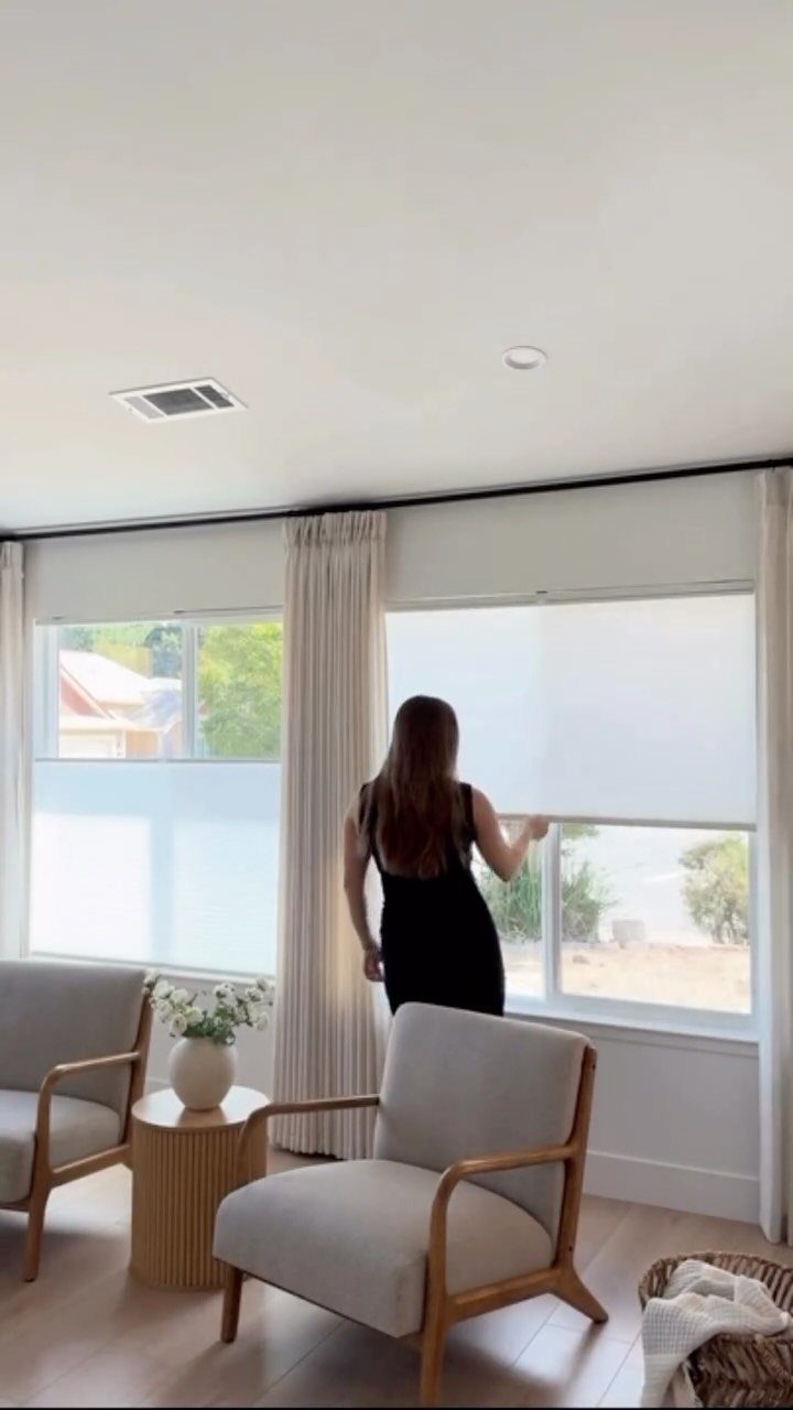 10 Window Dressing Ideas for Shutters, Shades and Blinds 6 A woman adjusts a white roller shade on a large window in a bright room.