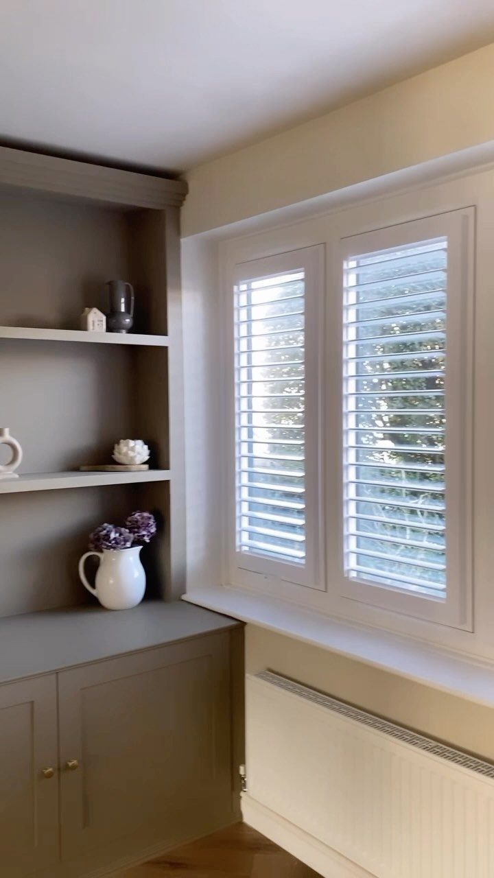 10 Window Dressing Ideas for Shutters, Shades and Blinds 1 White plantation shutters installed on a window next to built-in grey shelving units.