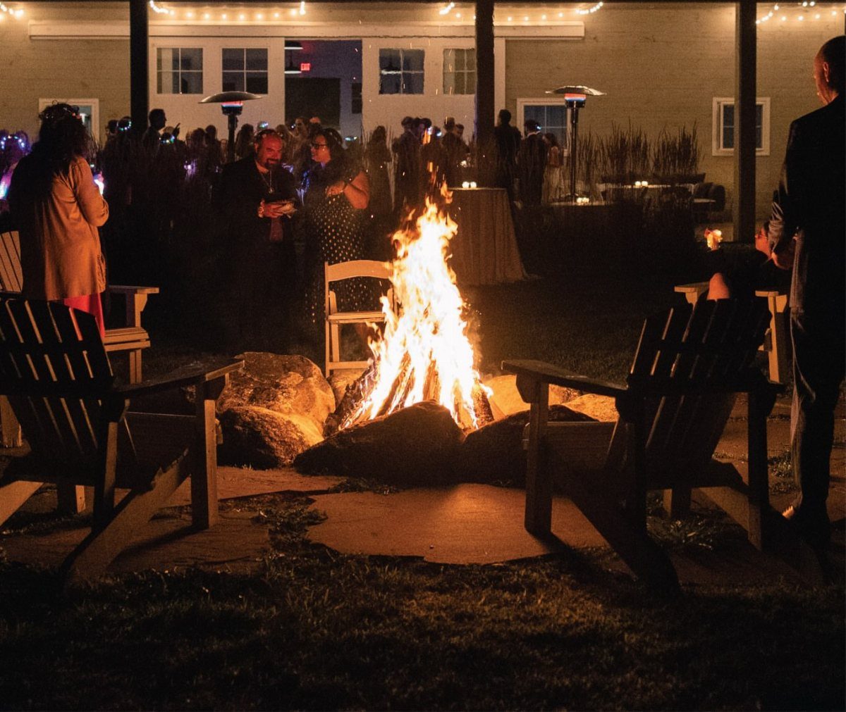 A bright bonfire burning in a stone fire pit surrounded by wooden Adirondack chairs at night.