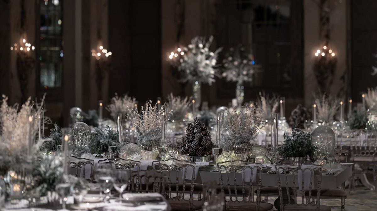 Elegant wedding reception tables featuring frosted floral centerpieces and glowing candles in a dim ballroom.