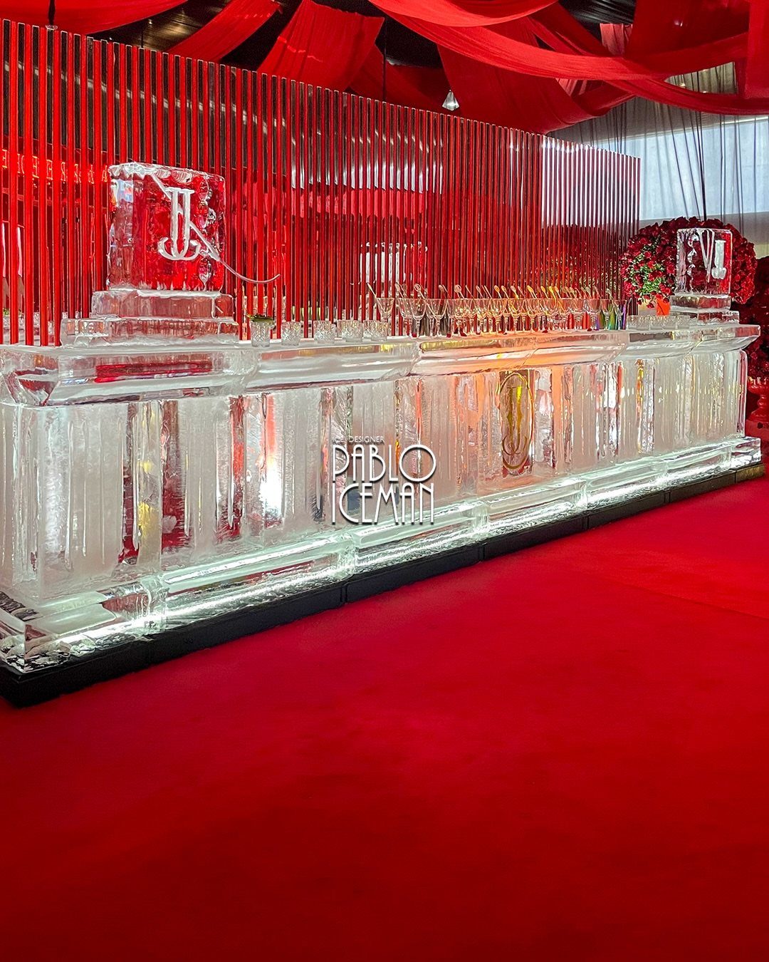 A long bar constructed from clear ice blocks set against a red backdrop and red carpet.