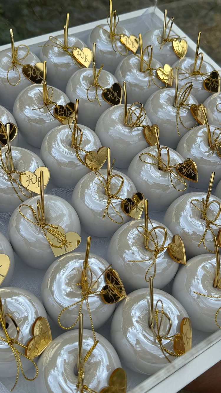 White glossy candy apples decorated with gold bows and heart charms in a white tray.