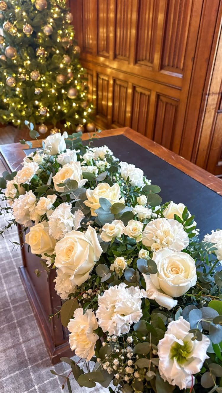 White roses and carnations with green eucalyptus leaves arranged on a dark wooden table.