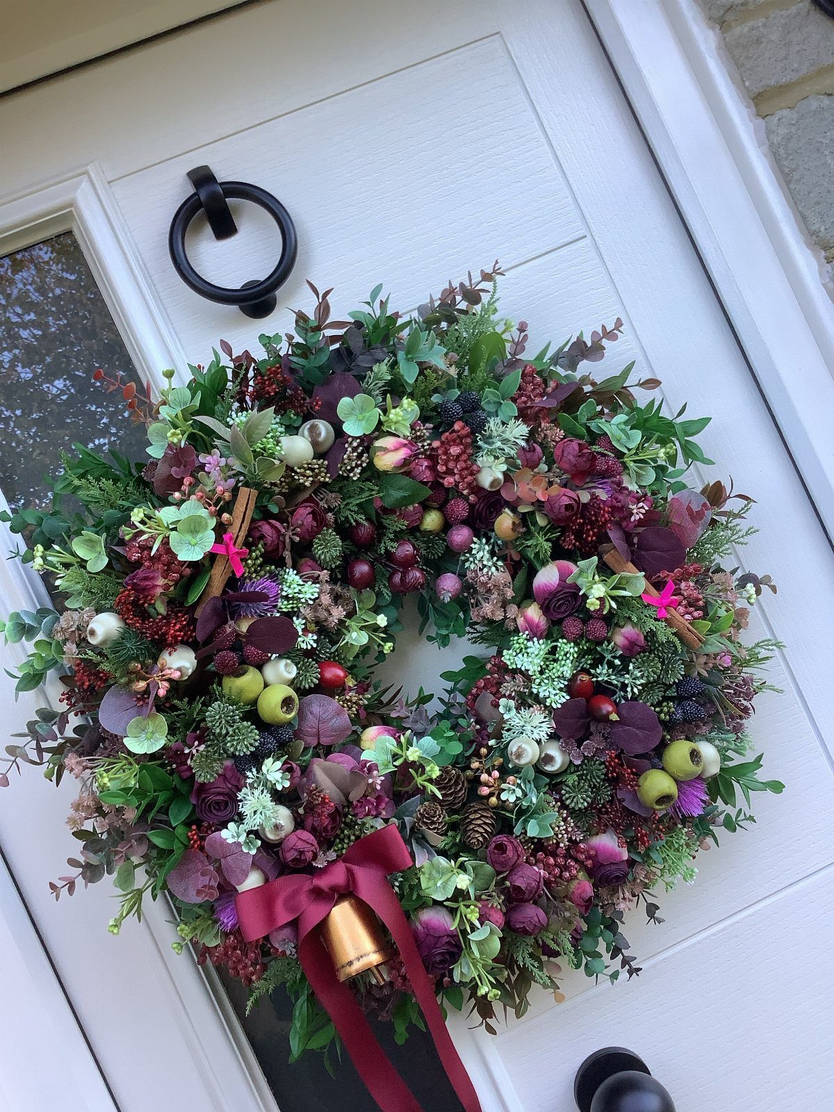 32 Xmas Gifts to Make: Easy Ideas for Handmade Holiday Presents 3 A lush Christmas wreath with red berries and a gold bell hanging on a white door.