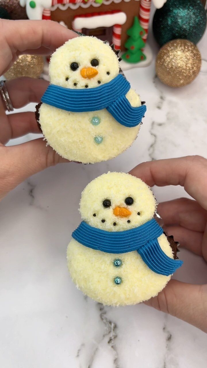 32 Xmas Gifts to Make: Easy Ideas for Handmade Holiday Presents 11 Two hands holding cupcakes decorated as snowmen with blue frosting scarves and orange noses.