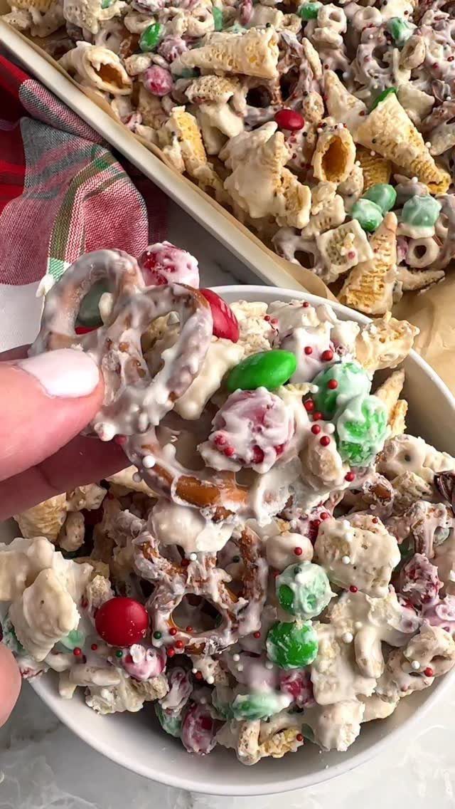 32 Xmas Gifts to Make: Easy Ideas for Handmade Holiday Presents 28 A hand holds a cluster of white chocolate covered snack mix with red and green candies.