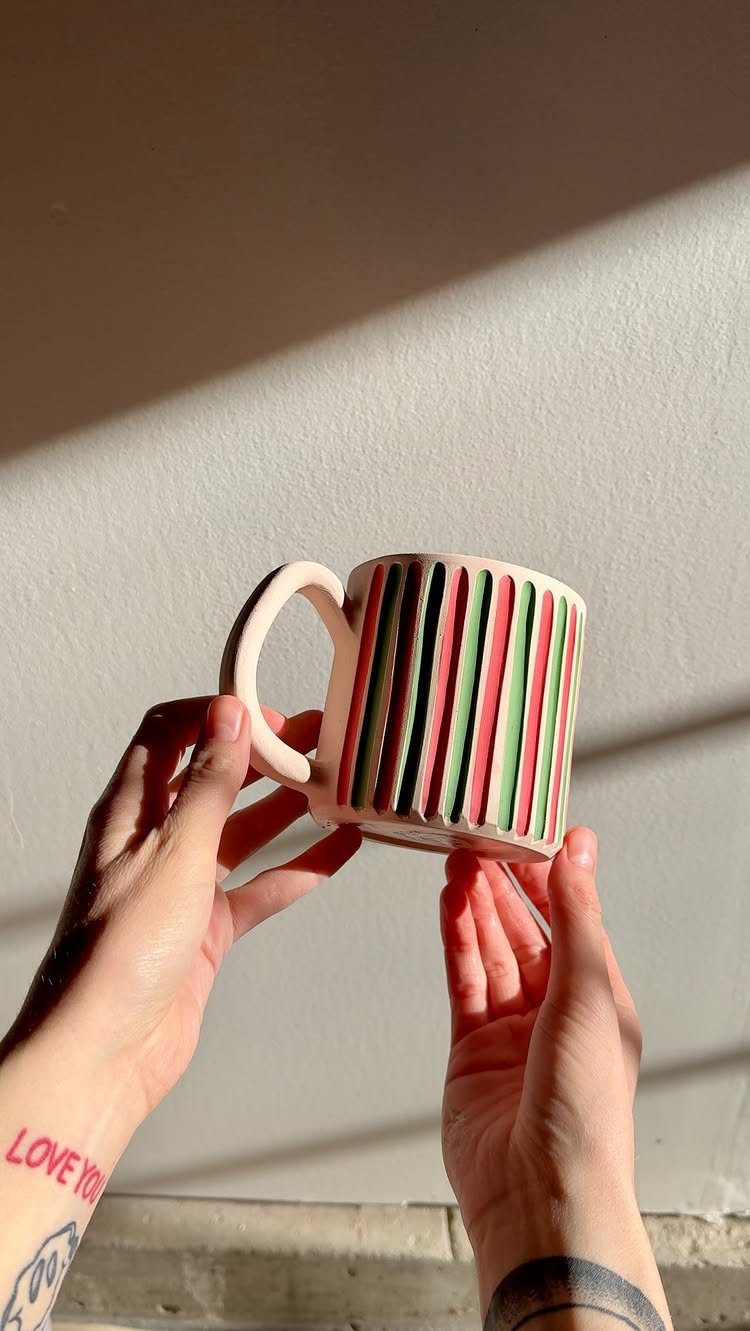 32 Xmas Gifts to Make: Easy Ideas for Handmade Holiday Presents 15 Hands holding a ceramic mug decorated with vertical red, green, and cream stripes.