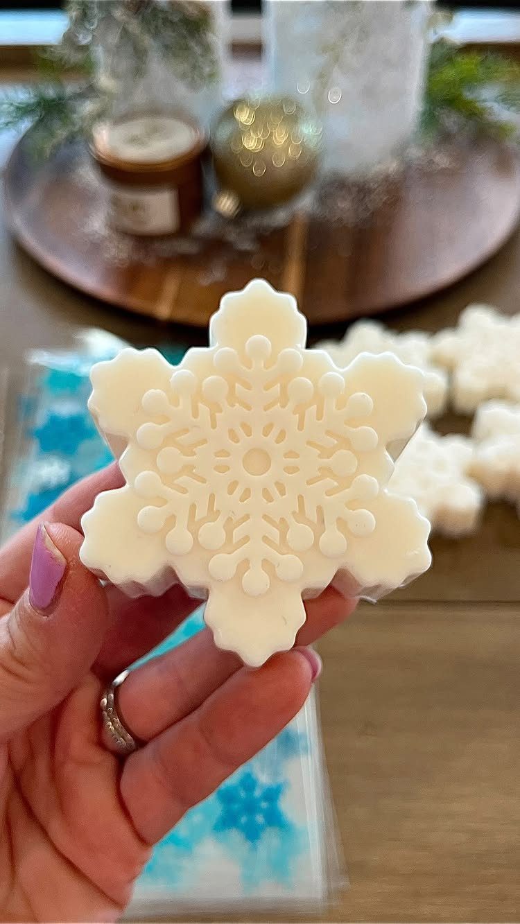 32 Xmas Gifts to Make: Easy Ideas for Handmade Holiday Presents 31 A hand holding a white snowflake-shaped soap against a blurred festive background.