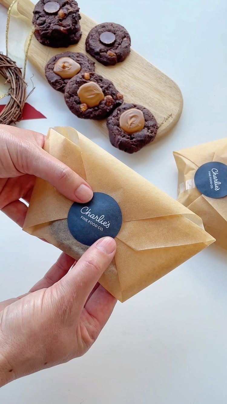 32 Xmas Gifts to Make: Easy Ideas for Handmade Holiday Presents 24 Hands holding a brown paper gift bag with dark chocolate cookies on a wooden board behind it.