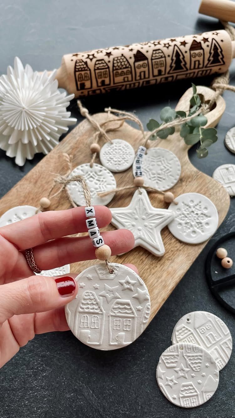 32 Xmas Gifts to Make: Easy Ideas for Handmade Holiday Presents 19 A hand holding a white salt dough ornament with embossed house designs on a wooden board.