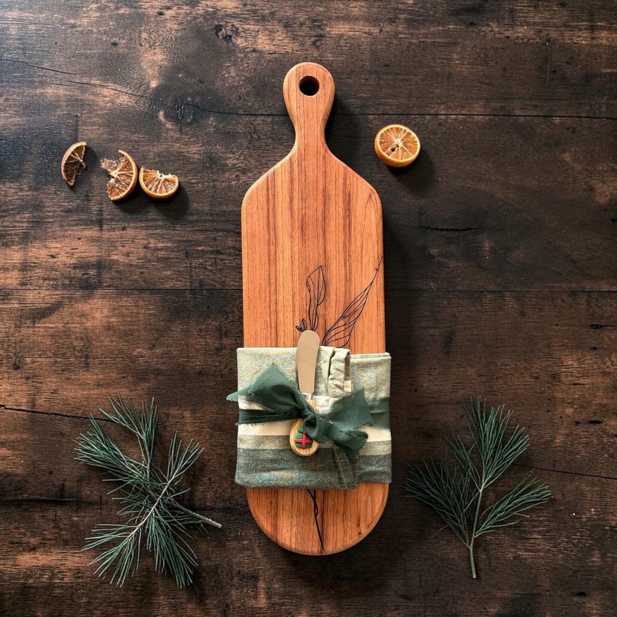 32 Xmas Gifts to Make: Easy Ideas for Handmade Holiday Presents 16 A wooden paddle cutting board with a folded cloth napkin tied to it on dark wood.