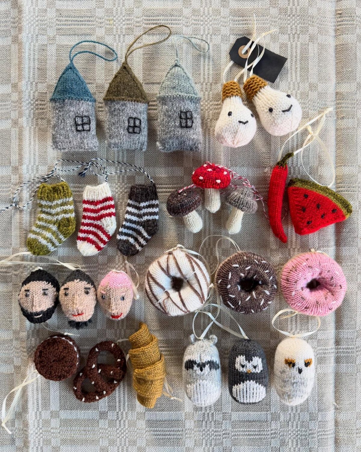 32 Xmas Gifts to Make: Easy Ideas for Handmade Holiday Presents 6 Handmade knitted ornaments shaped like houses, food, and animals resting on a grey fabric surface.